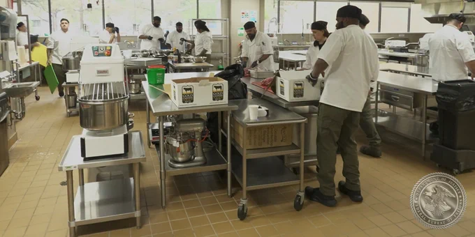 Group of individuals in in a kitchen wearing kitchen uniforms unboxing food and preparing to cook.