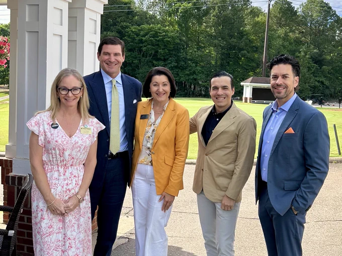 Five people in business attire smiling at the camera outside.