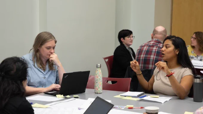 People with laptops, pens and paper having an animated discussion at a round table.