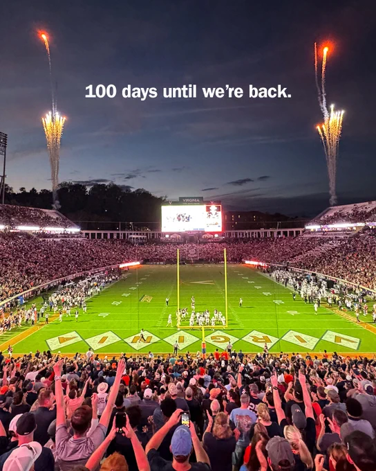 A crowded Scott Stadium with a game in progress, featuring fireworks in the evening sky. The scoreboard is lit up, and text at the top reads, "100 days until we’re back."
