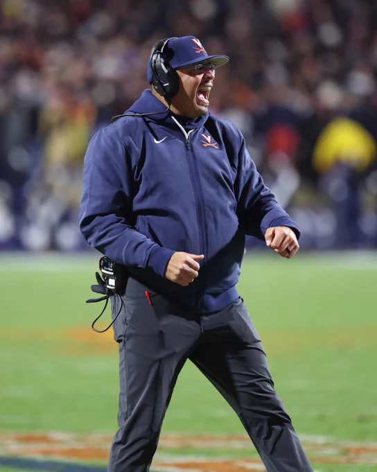 UVA football coach Tony Elliott wearing a headset and UVA apparel while energetically shouting.