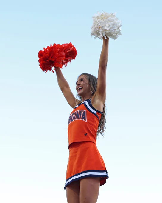 A cheerleader wearing an orange Virginia uniform holds pom-poms in the air.