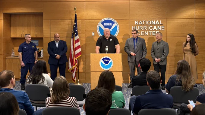 Speaker at podium with NOAA logo addressing audience at National Hurricane Center press event.