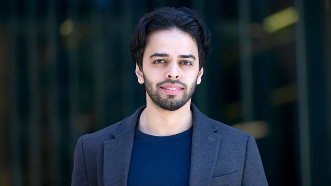 Abdul Mohammed (MBA '26) wearing a dark blazer over a navy blue shirt standing in front of a building. 