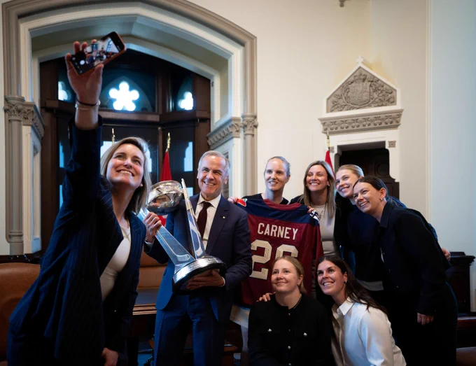 Prime Minister Mark Carney lifts the Walter Cup as he poses with members of the Montréal Victoire for a selfie taken by Marie-Philip Poulin.