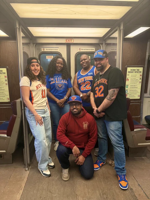Five LIRR employees wearing Knicks merch, posed inside of an LIRR M3 train, in front of the door.