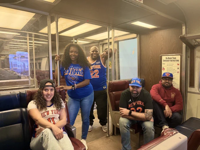 Five LIRR employees wearing Knicks merch, posed inside of an LIRR M3 train.