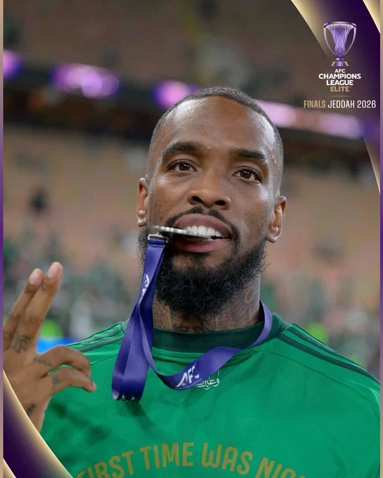 A football player celebrates after winning the AFC Champions League. He holds a medal in his mouth, showcasing a victorious moment.