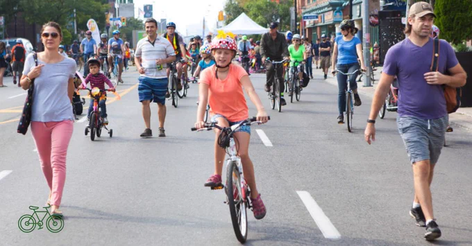 A busy city street filled with people walking and cycling on a sunny day, showcasing an active urban environment.