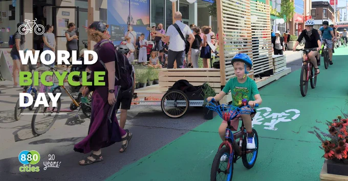Children and adults cycling and walking along a green bike lane in a busy urban area.