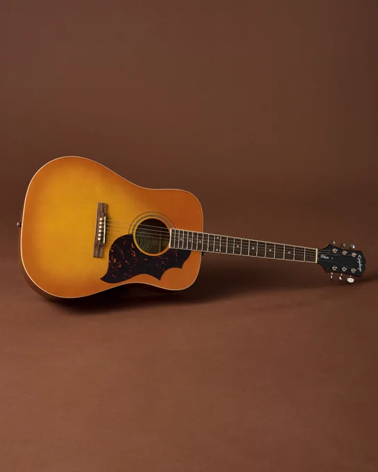 Acoustic Epiphone Hummingbird Tribute guitar with a sunburst finish, resting against a plain brown background.