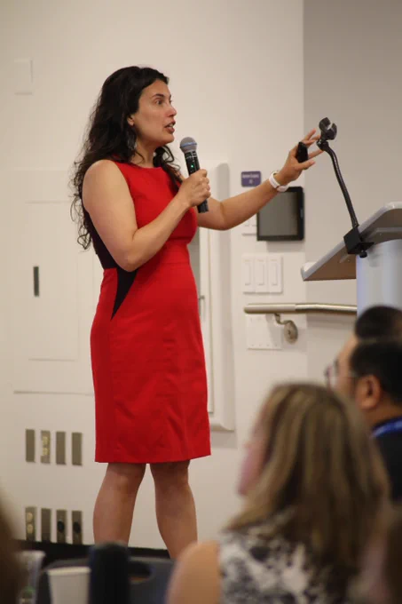 Dr. Emily Ragan speaks into a microphone while adjusting a microphone stand on a podium.