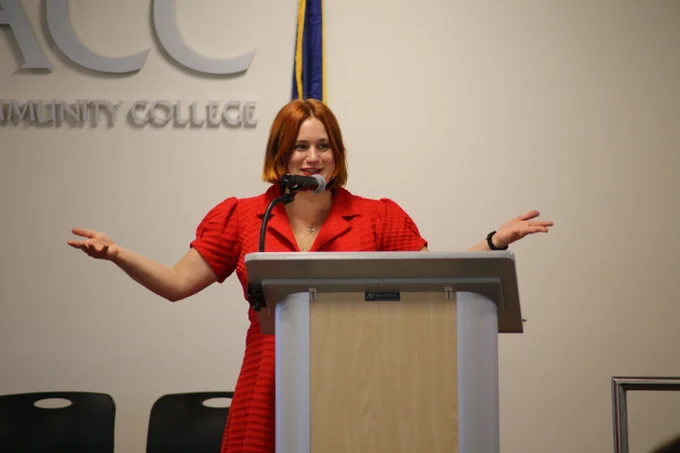 Chealsye Bowley speaks into a microphone at a podium with her arms extended in a gesture.