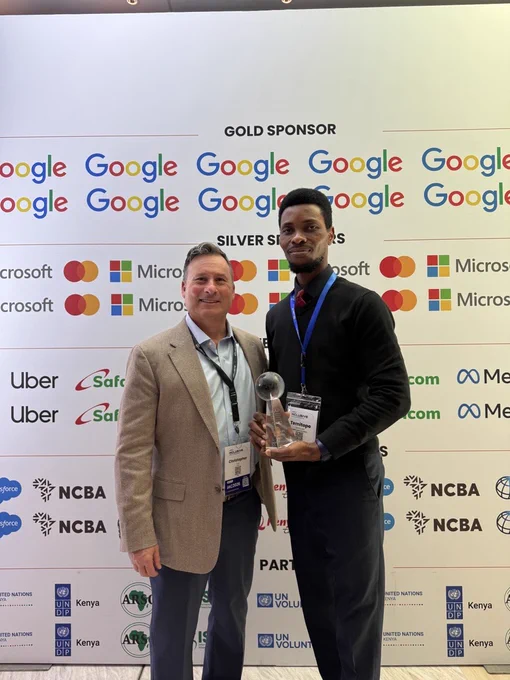 Dr. Christopher Michael Lee and Temitope Somuwa, MBA, CPACC, pose for a photo in front of the 2026 Inclusive Africa sponsor step-and-repeat. Temitope holds his 2025 IAAP Impact Award.