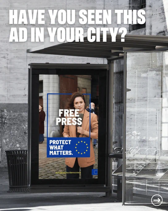 A bus shelter on a grey city street displays a digital advertisement showing a woman in a tan blazer holding a microphone, with the words Free Press and Protect What Matters alongside the European Union flag. Bold white text across the top of the image reads, Have you seen this ad in your city?