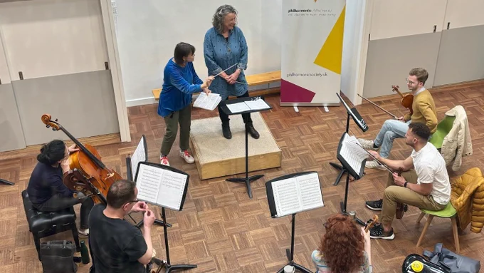 A participant at an RPS Conductors course, conducting an orchestra and receiving coaching from Alice Farnham.