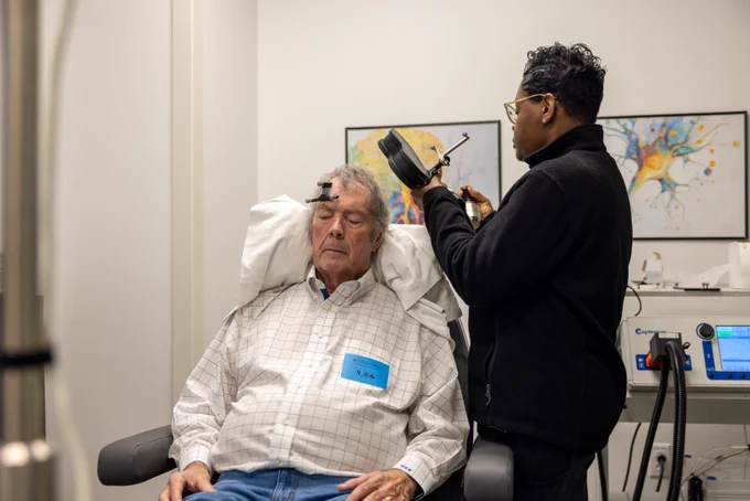 Bill Henderson receives Stanford Accelerated Intelligent Neuromodulation Therapy (SAINT) at the Center for Interventional Psychiatry at UTHealth Houston. A clinician positions the transcranial magnetic stimulation device near his head as he sits awake and relaxed during the treatment session.