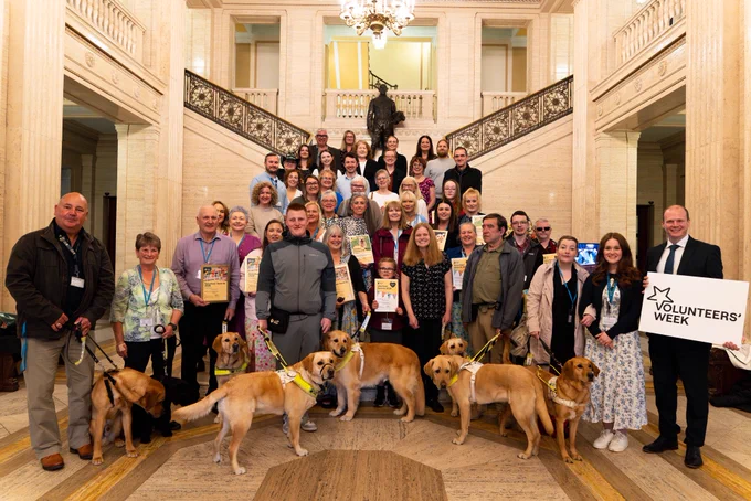 A group shot featuring Minister Lyons and Guide Dogs NI volunteers in the Great Hall in Parliament Buildings.