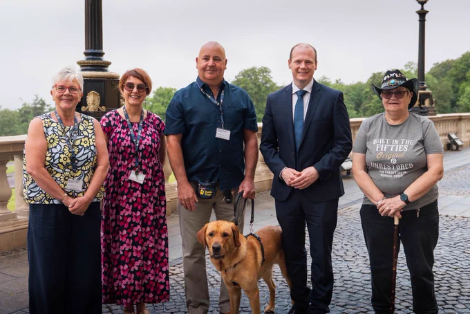 A group shot featuring Minister Lyons and Guide Dogs NI volunteers outside Parliament Buildings.