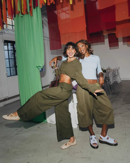 An image of two people wearing pairs of schuh and Dr Martens shoes with green and blue outfits whilst standing in a white room.