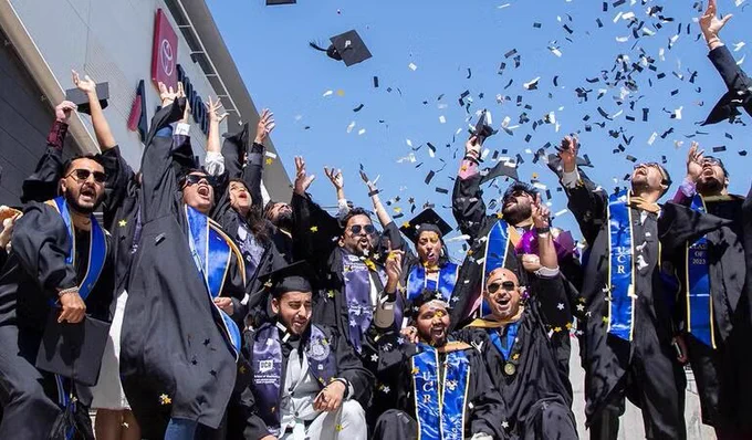 Students in caps & gowns in a large group throwing confetti