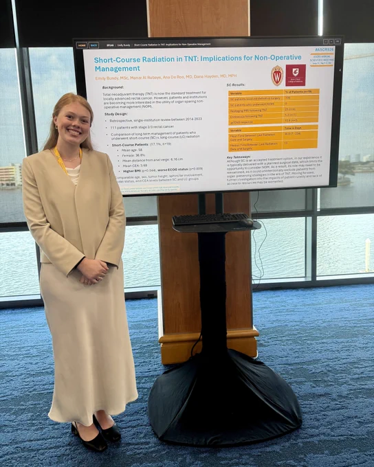 Emily Bundy stands next to a digital poster presentation titled "Short-Course Radiation in TNT: Implications for Non-Operative Management."