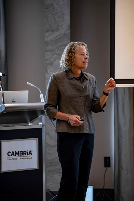 A professional stands, giving a presentation next to a podium in a conference room.
