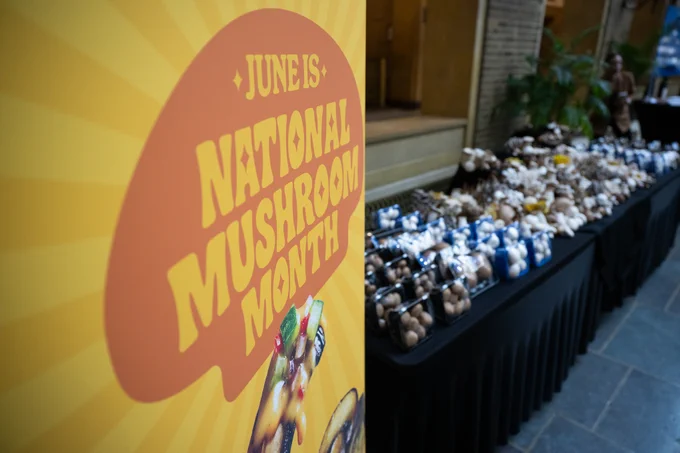 Banner displaying "June is National Mushroom Month" beside a table filled with various packages of mushrooms.