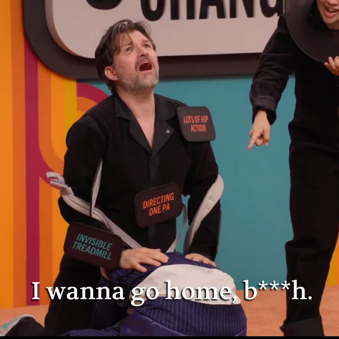 A man in a black outfit theatrically expresses frustration while another person gestures towards him, both surrounded by colorful accents.