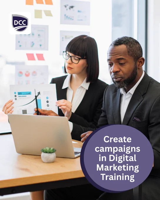 Two business professionals sit at a meeting table reviewing charts beside a laptop while promotional text references creating campaigns through Digital Marketing training at Discovery Community College.