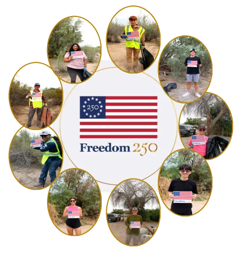 Volunteers holding Freedom 250 signs while cleaning a natural outdoor area with trees and dirt paths.