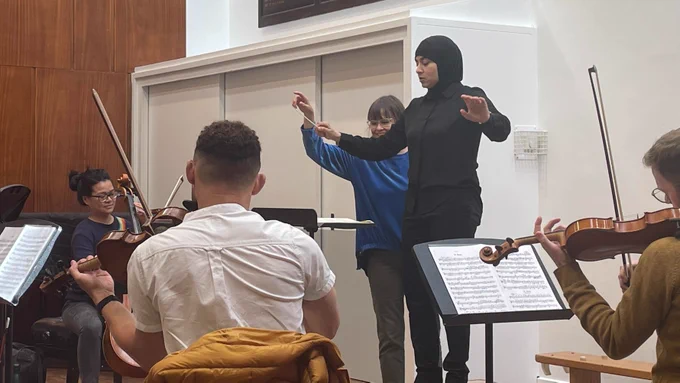 A participant at an RPS Conductors course, conducting an orchestra and receiving coaching from Alice Farnham.