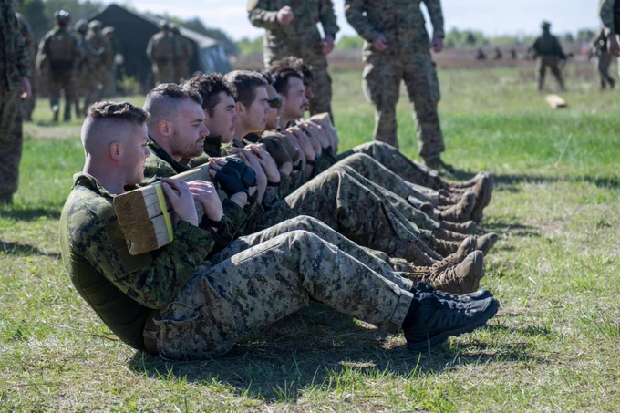 A group of soldiers performing sit-up exercises outdoors on grass during military training.