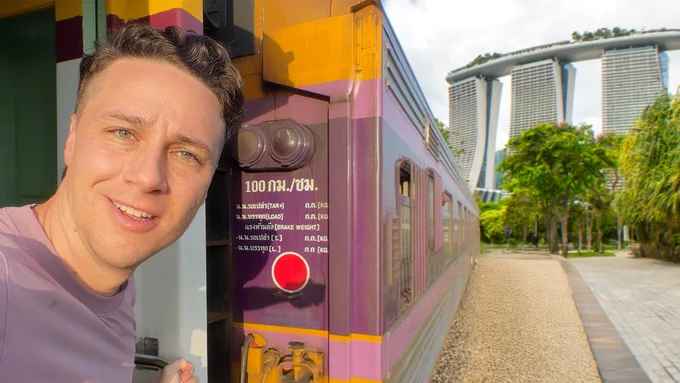 Michael Downie looks into the camera on a train to Singapore, the iconic Marina Bay Sands hotel in the background.