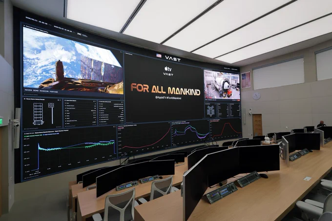 A photo of the Vast Space Station Mission Control room. There are various computer screens on desks. At the very front of the room is a screen projecting “For All Mankind.”