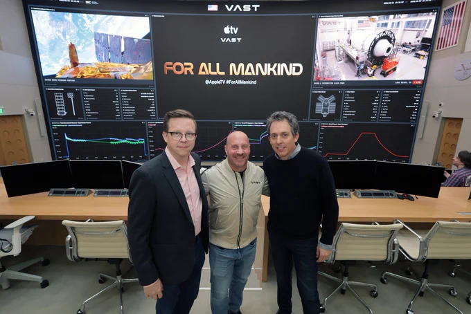 Ben Nedivi, Matt Wolpert, and Garrett Reisman pose for a photo together at Vast Space Station mission control room. Behind them is a screen that is projecting “For All Mankind.”