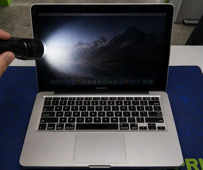 MacBook screen tested with flashlight revealing faint image, illustrating backlight failure and common diagnosis for dim or black display issues.