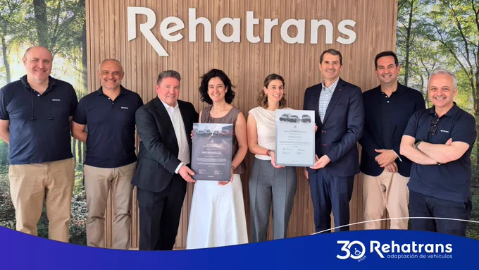 Nueve personas frente al logo Rehatrans, dos en el centro sostienen certificados; ambiente corporativo de celebración.