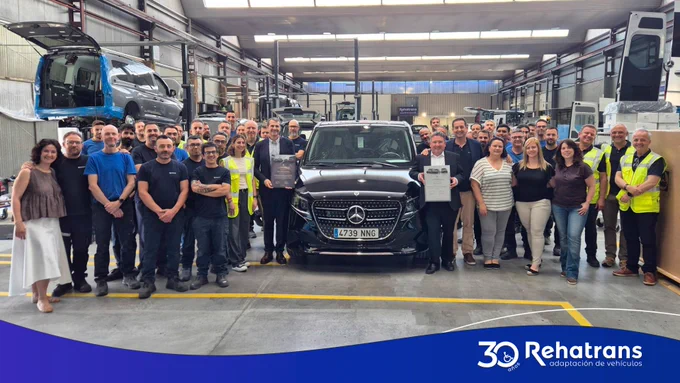 Equipo de Rehatrans posando en taller alrededor de una furgoneta Mercedes negra, celebrando 30 años con certificados.