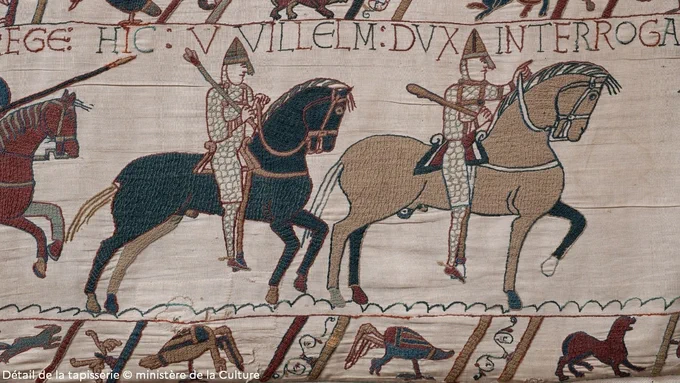Détail de la tapisserie de Bayeux représentant des cavaliers revétus de cottes de maille et casqués, se dirigeant vers la droite. Les personages sont surmontés d'une légende en latin décrivant la scène. La broderie principale est bordée en haut et en bas de frises représentant des animaux.
Détail de la tapisserie © ministère de la Culture