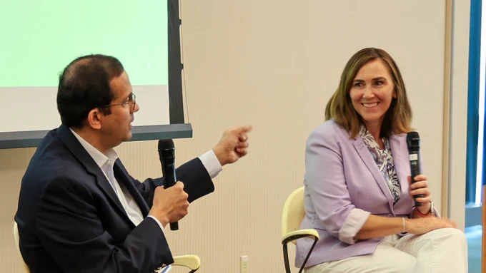 Arjun Shankar gestures while speaking into a microphone during a leadership panel discussion as Ashley Barker listens and smiles.