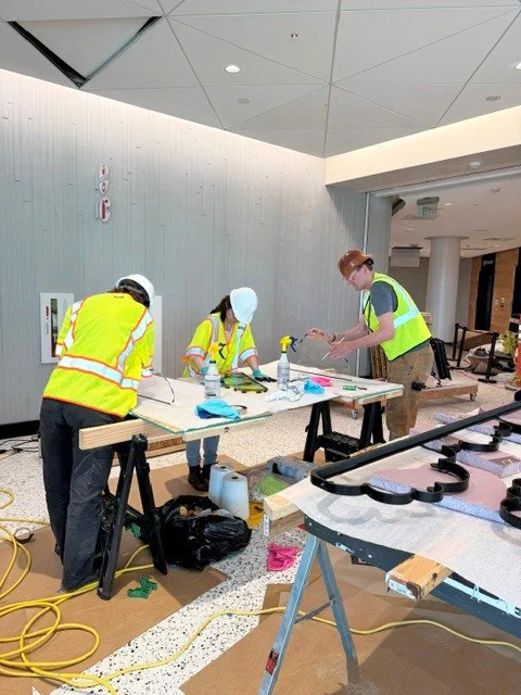 Three workers in high-visibility vests perform tasks at a worktable in a construction area.