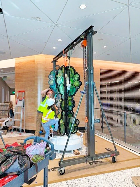 Two construction workers assembling a green glass panel installation indoors.