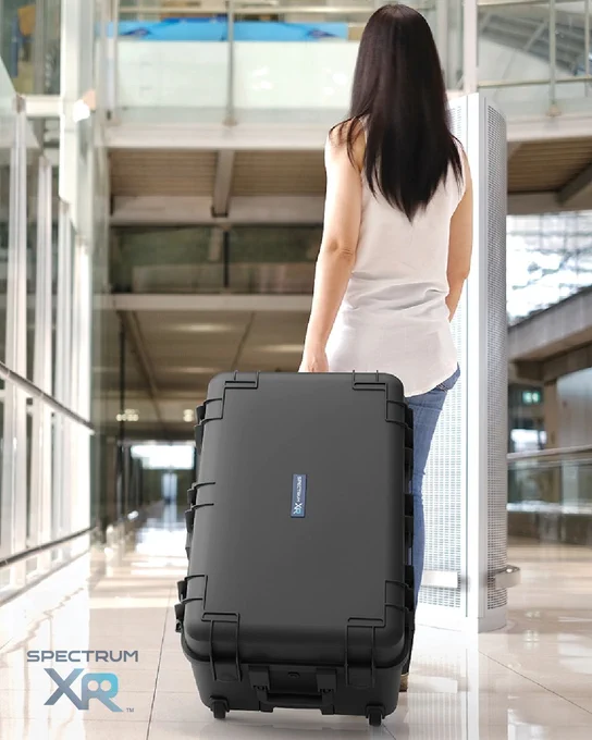 Traveler pulling a rugged, crush-resistant VR case with retractable handle and wheels through an airport corridor.
