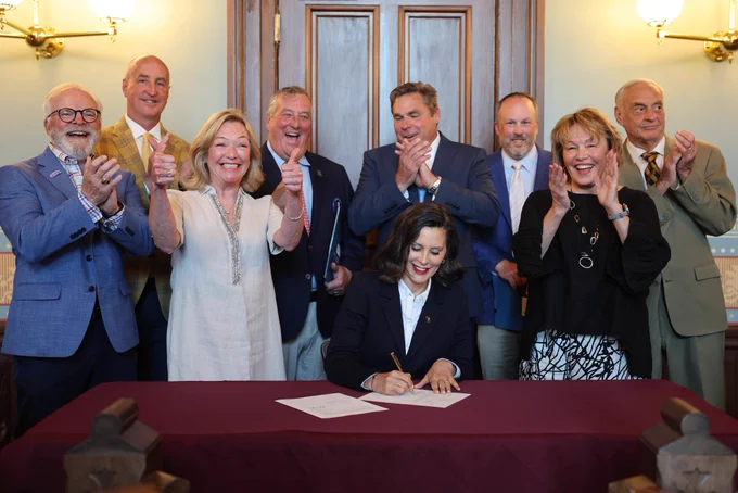 Gov. Whitmer signs a bill with community leaders behind her.