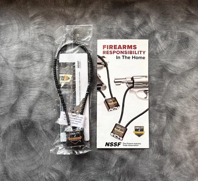 Firearm cable lock with keys and a brochure titled 'Firearms Responsibility In The Home' from the NSSF on a textured surface.