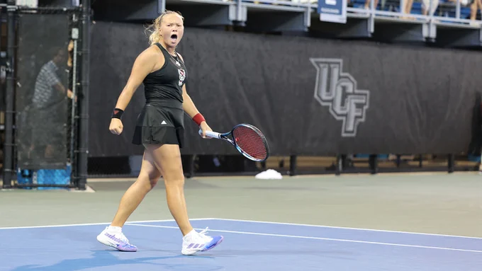 Diana Shnaider in black NC State athletic wear walking on a blue and green tennis court.
