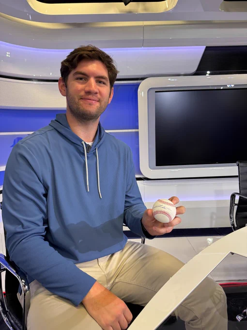 Gavin Williams holds an autographed baseball. He wears a blue hoodie and khaki pants.