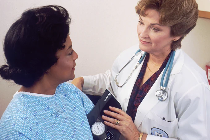 A healthcare professional holds a blood pressure device, checking the blood pressure of a female patient. 