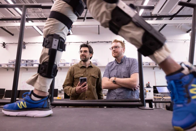 Two men observe a motorized knee exoskeleton during a research session.
